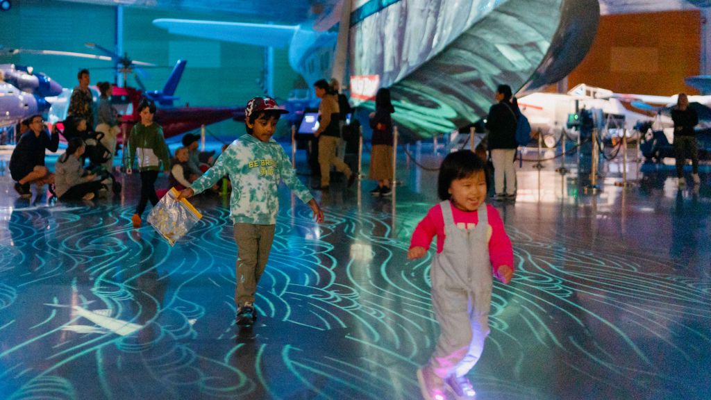 Children under blue light projections with airplanes in the background.